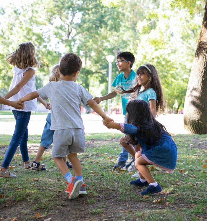 Happy children playing together outdoors, dancing around on grass, enjoying outdoor activities and having fun in park. Kids party or friendship concept